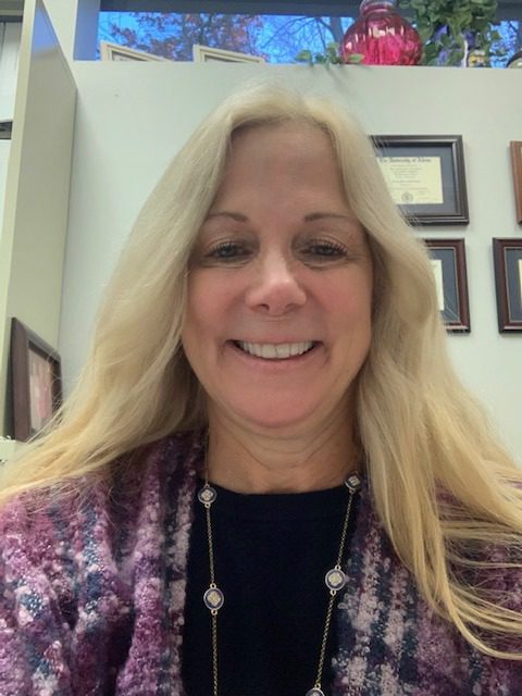 A woman with long blonde hair smiling in an office.