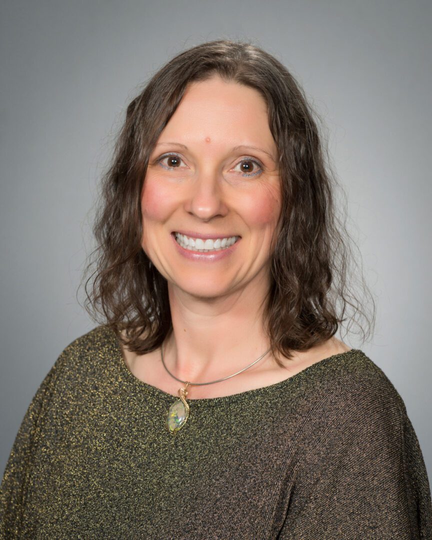 A woman with long hair and a necklace smiles for the camera.