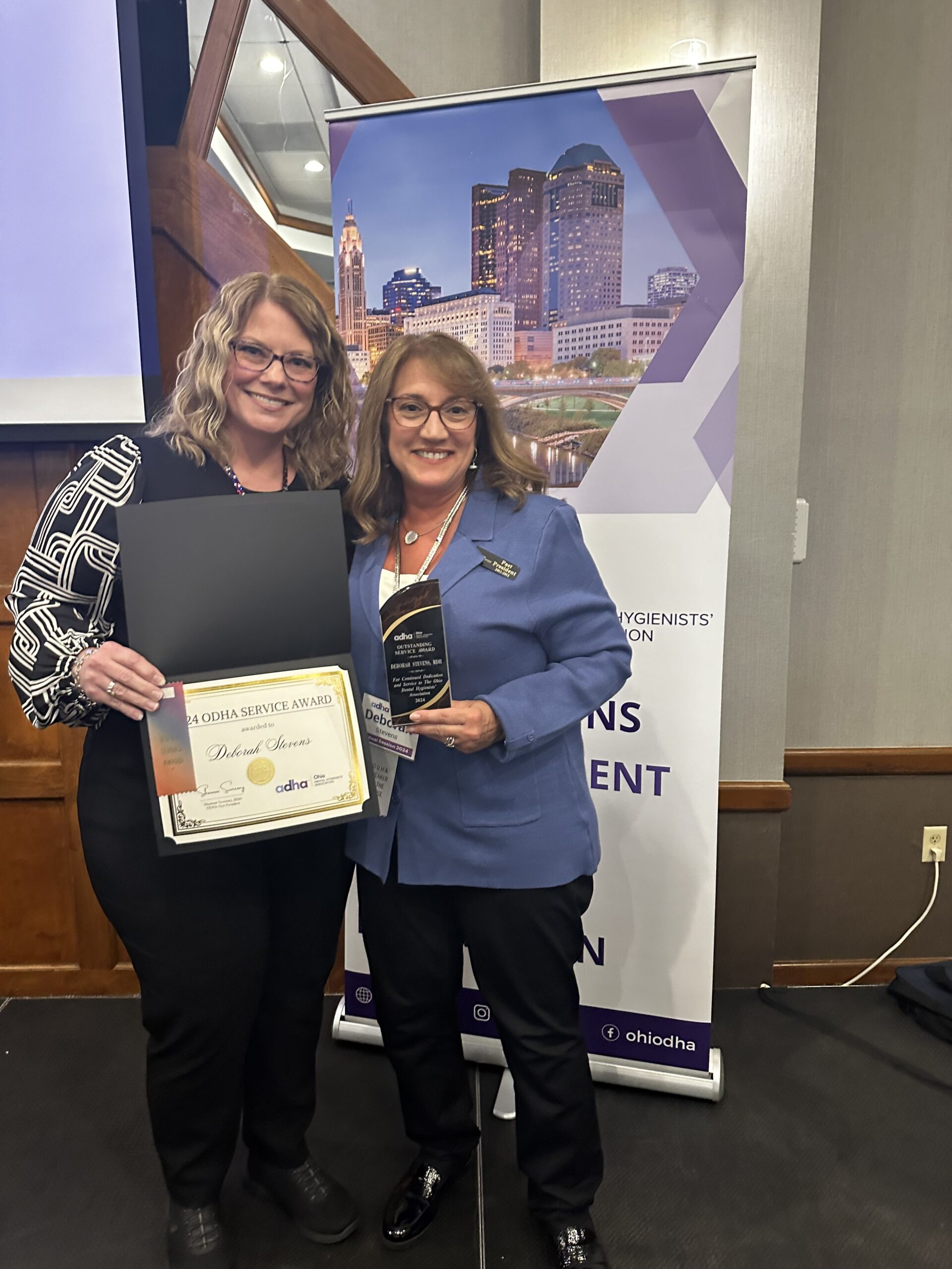 Two women holding a plaque and an award.